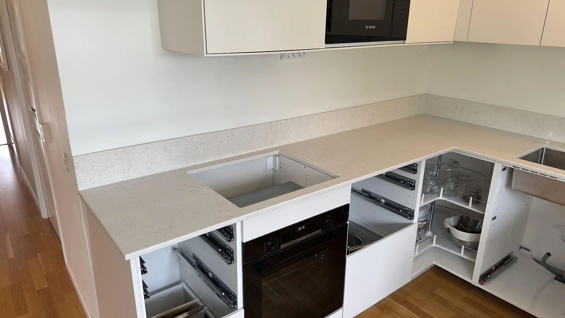 Närbild på polerad Silestone Snowy Ibiza som köksbänkskiva med hällöppning, uppvikt stänkskydd och öppna köksstommar i Västerås.