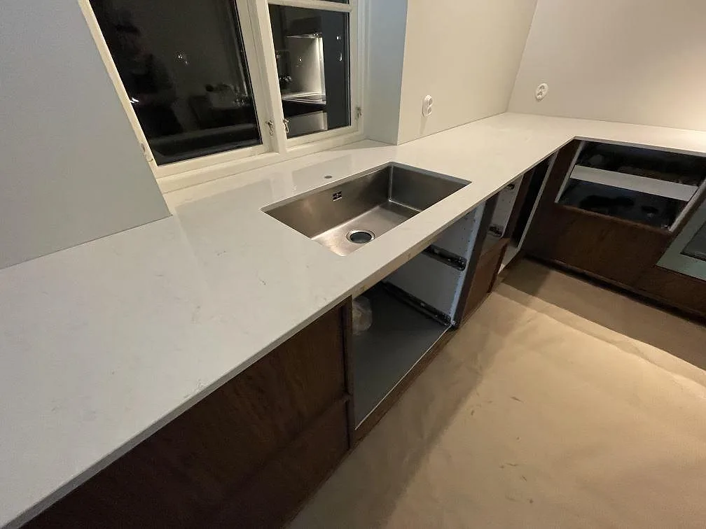 Köksbänkskiva i vit Silestone Snowy Ibiza, polerad komposit, med underlimmad rostfri diskho under fönstret i ett kök under montering i Västerås.