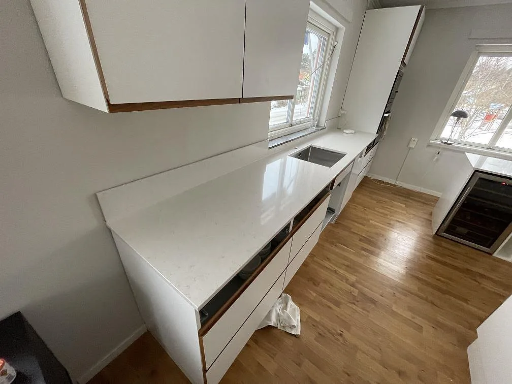 Polerad köksbänkskiva i Silestone Snowy Ibiza med underlimmad rostfri diskho under fönstret i ett kök i Västerås.