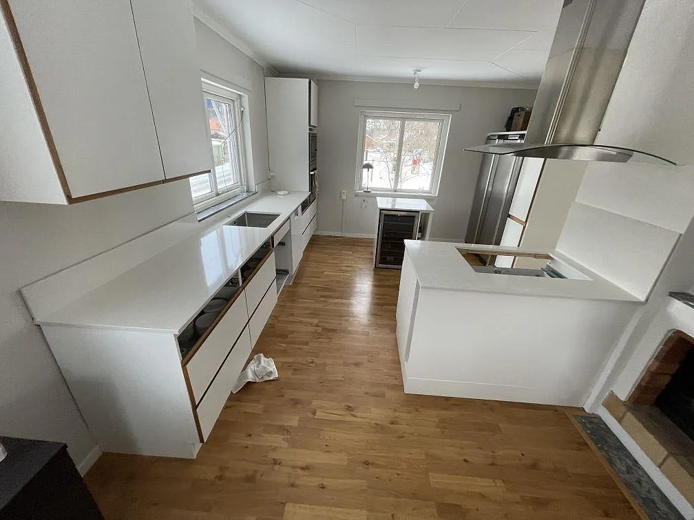 Köksbänkskiva i vit Silestone Snowy Ibiza, polerad, med L-formad bänkrad och fristående halvö med urtag för häll i ett kök i Västerås.
