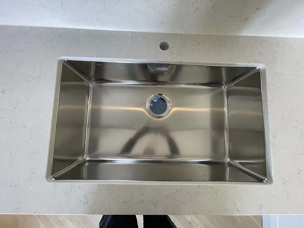 Underlimmad rostfri diskho infälld i vit Silestone Snowy Ibiza bänkskiva med synlig grå ådring i ett kök i Västerås.