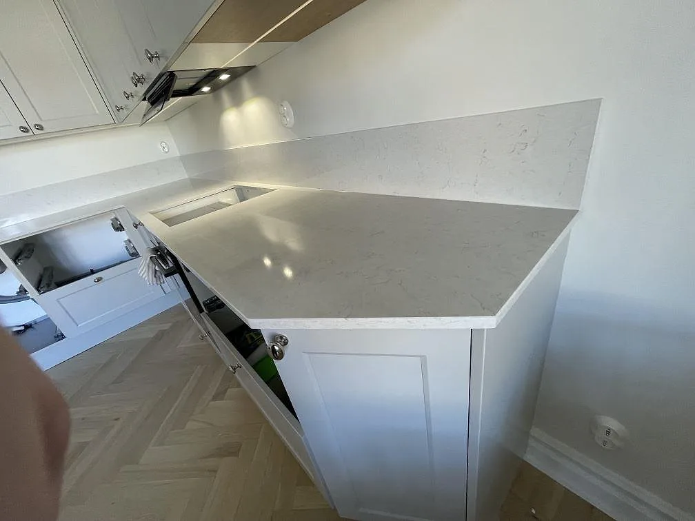 Polerad köksbänk i Silestone Snowy Ibiza med fasad hörnskiva och uppvikt stänkskydd, monterad i ett ljust kök i Västerås.