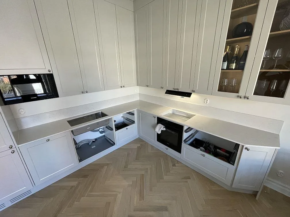 Köksbänkskiva i vit Silestone Snowy Ibiza, polerad, med mjuk grå ådring och matchande stänkskydd i ett vinklat kök under montering i Västerås.