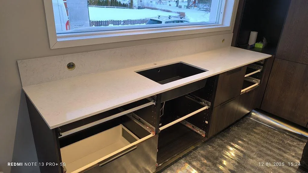 Polerad köksbänkskiva i Silestone Snowy Ibiza, 20 mm, med uppvikt stänkskydd och öppning för diskho i ett kök i Västervik.
