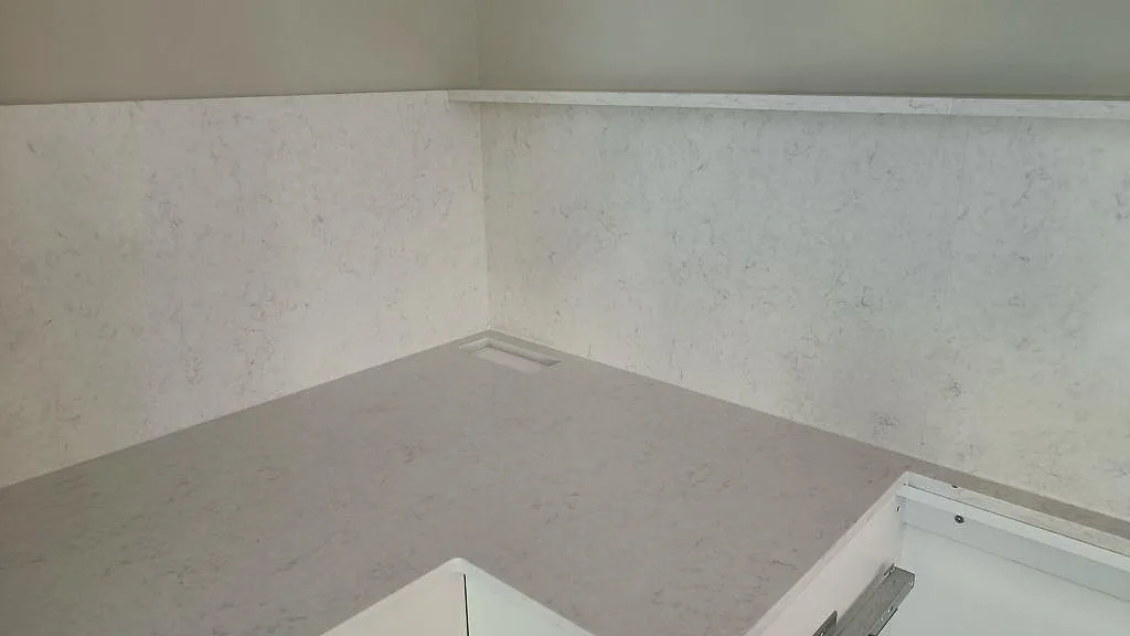 Hörnvy över polerad Silestone Snowy Ibiza med stänkskydd, hälluttag och diskzonen under montering i Västra Frölunda.