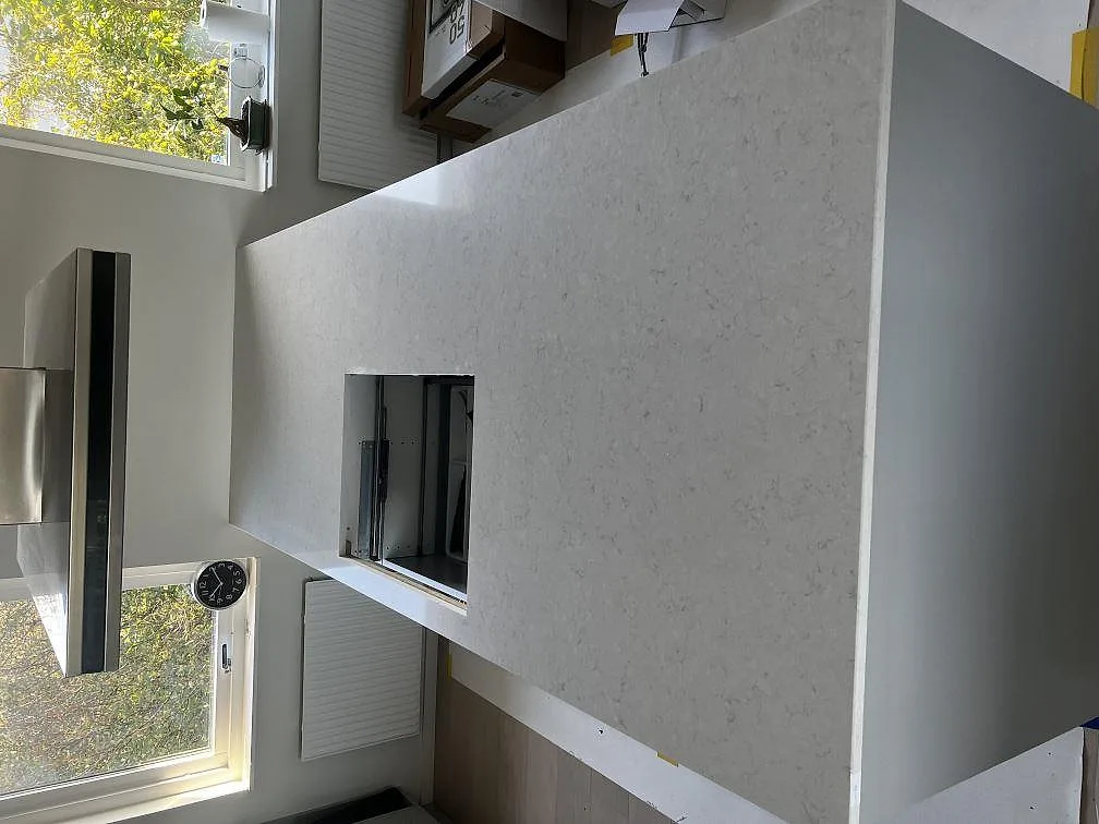 Närbild av stor köksö i polerad Silestone Snowy Ibiza komposit med ljus grå ådring och utskärning under montering i Västra Frölunda.