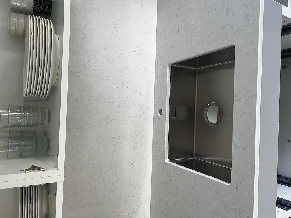 Detalj av rostfri diskho i polerad Silestone Snowy Ibiza komposit med ljus stenbild och öppet köksskåp i Västra Frölunda.