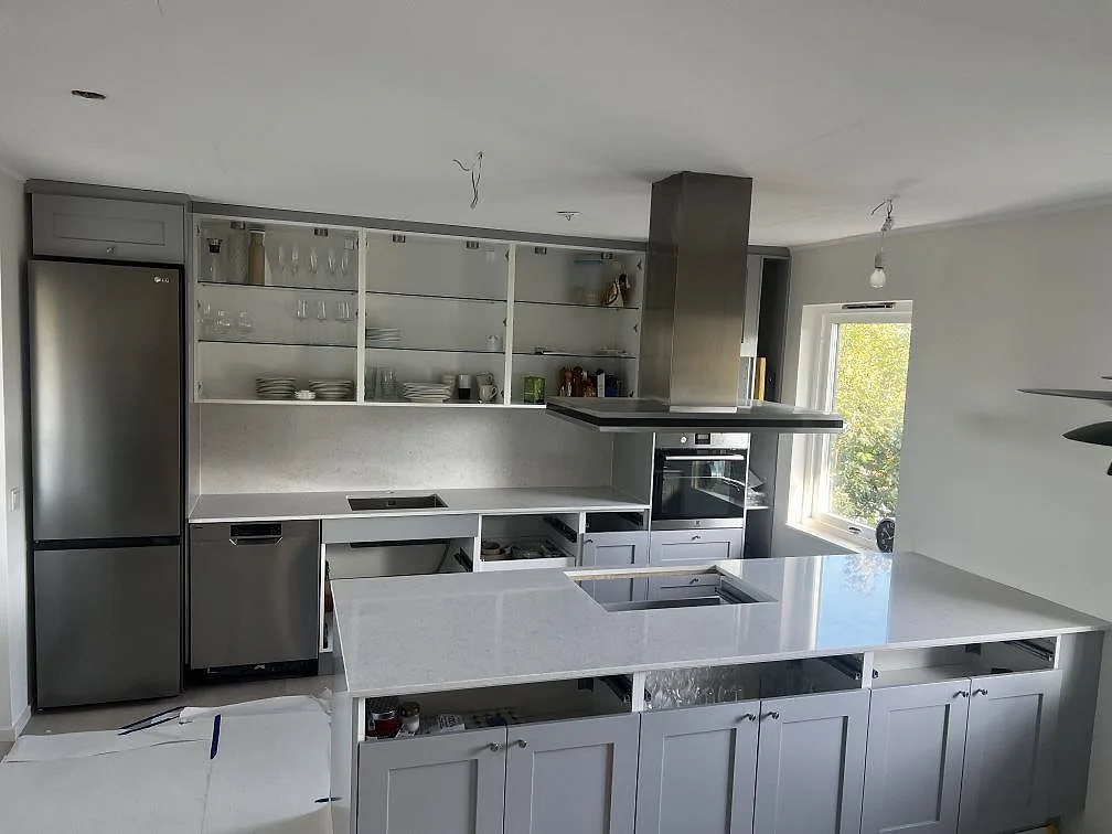 Köksbänkskiva och stor köksö i polerad Silestone Snowy Ibiza komposit med svart induktionshäll i ett kök i Västra Frölunda.