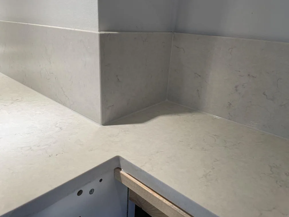 Hörndetalj med köksbänkskiva och uppvikt stänkskydd i polerad Silestone Snowy Ibiza under montering i Västra Frölunda.