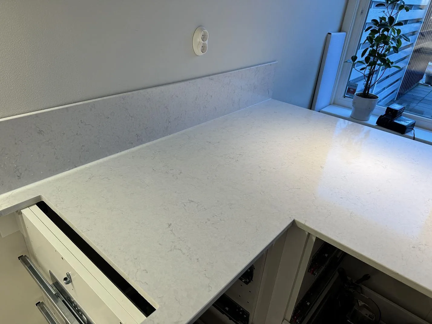 Polerad Silestone Snowy Ibiza som L-formad arbetsyta med uppvikt stänkkant vid fönster i ett kök i Västra Frölunda.
