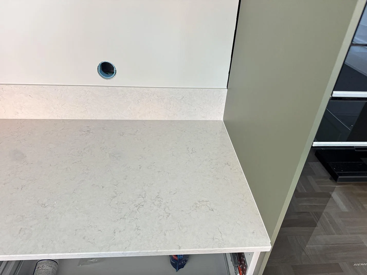 Detalj av polerad Silestone Snowy Ibiza kvartskomposit med lågt stänkskydd och grön skåpsida i Västra Frölunda.