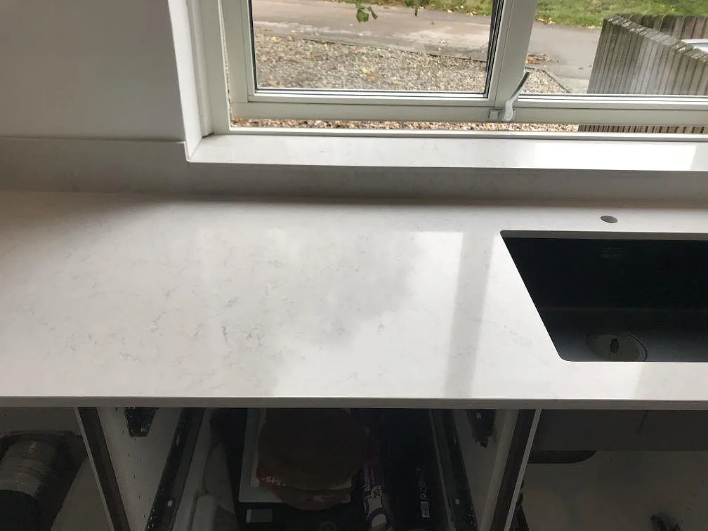 Polerad köksbänkskiva i Silestone Snowy Ibiza med underlimmad svart kompositdiskho och kranhål framför fönstret i ett kök i Växjö.