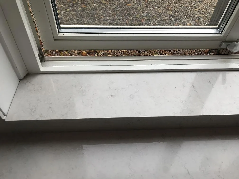 Köksbänkskiva i polerad Silestone Snowy Ibiza vid fönstret med underlimmad svart kompositdiskho i ett kök i Växjö.