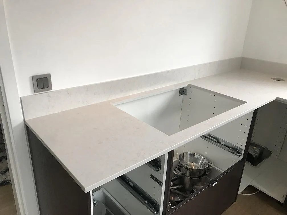 Närbild på den polerade köksbänkskivan i Silestone Snowy Ibiza med hålurtag för blandare och mjuk grå ådring i ett kök i Växjö.