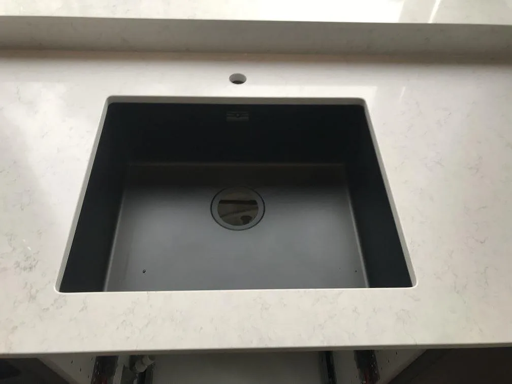Underlimmad svart kompositdiskho i en polerad köksbänkskiva i Silestone Snowy Ibiza i ett kök i Växjö.