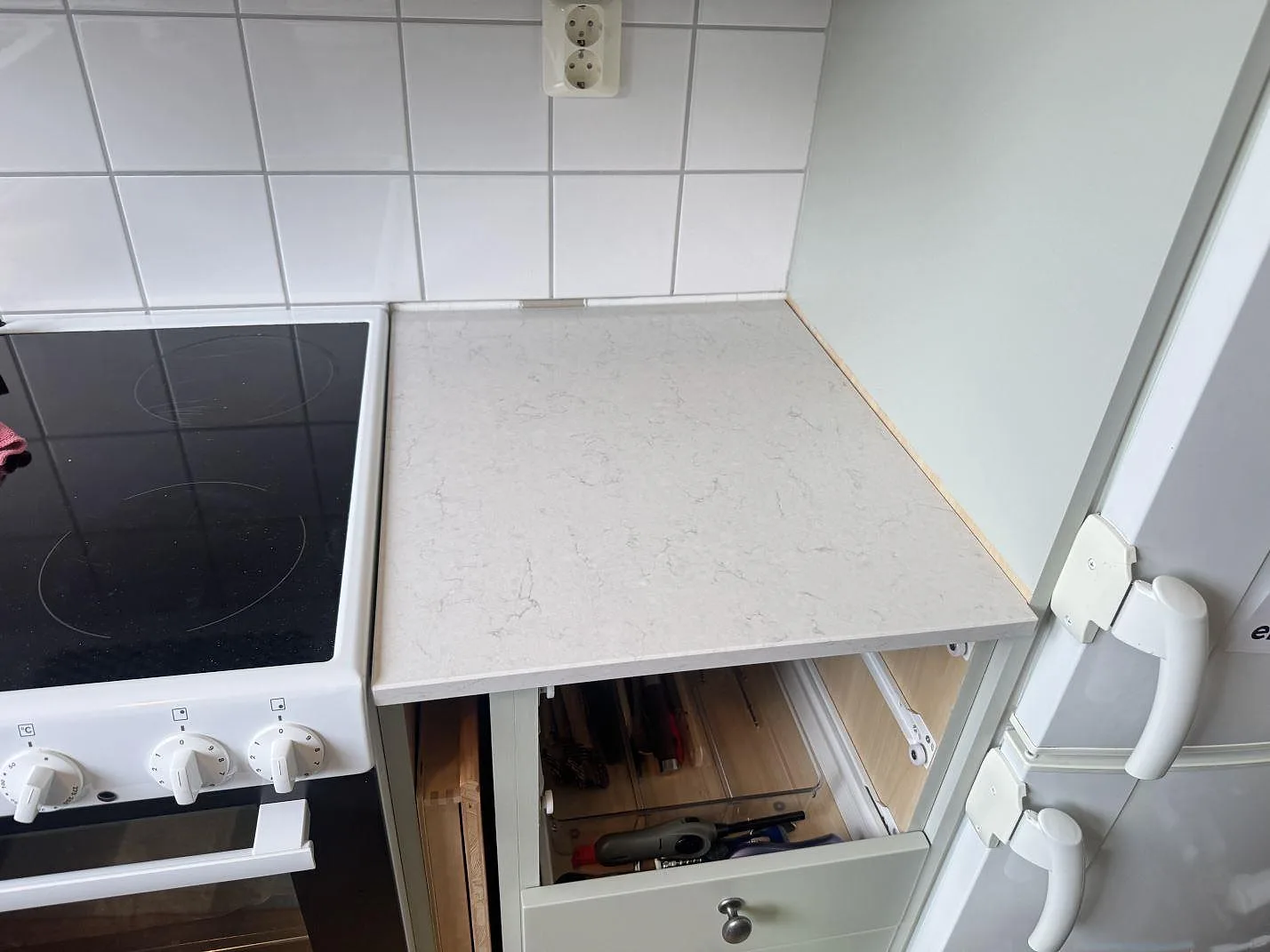 Kort köksbänk i polerad Silestone Snowy Ibiza bredvid fristående spis och ljus vägg i Växjö.