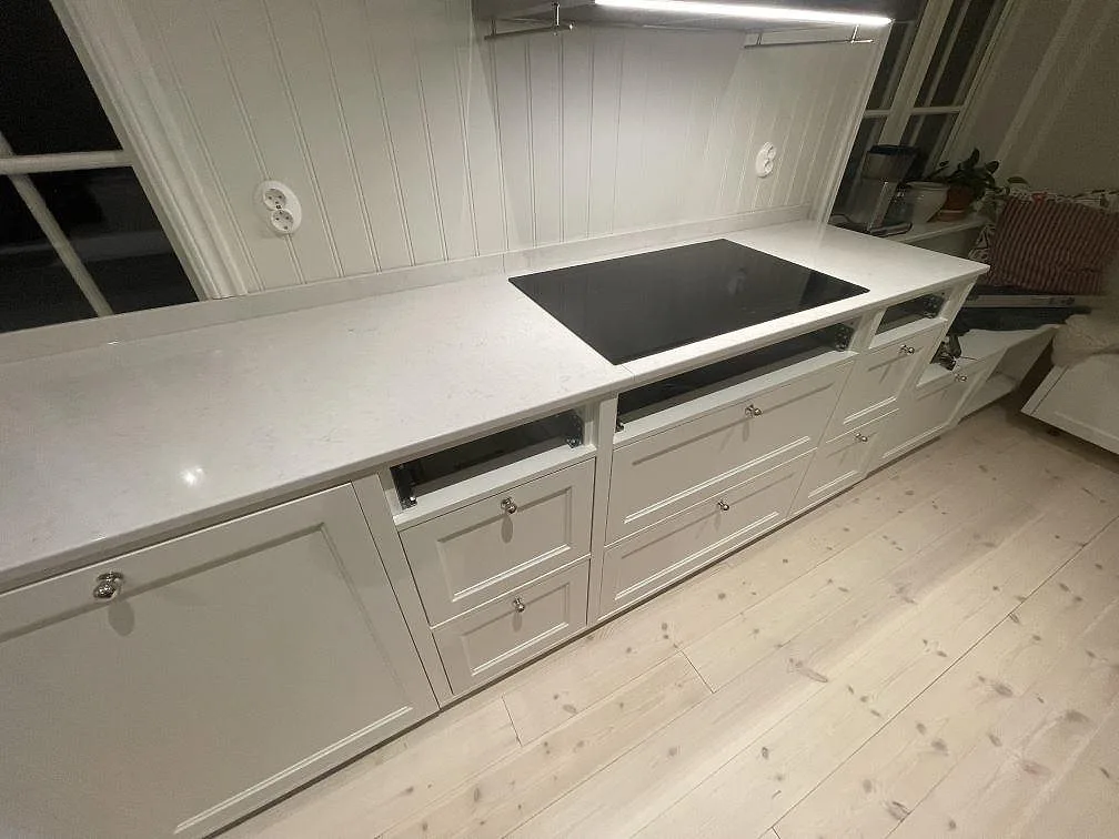 Polerad Silestone Snowy Ibiza köksbänkskiva med infälld induktionshäll och underbelysning längs väggen i ett kök i Vallentuna.