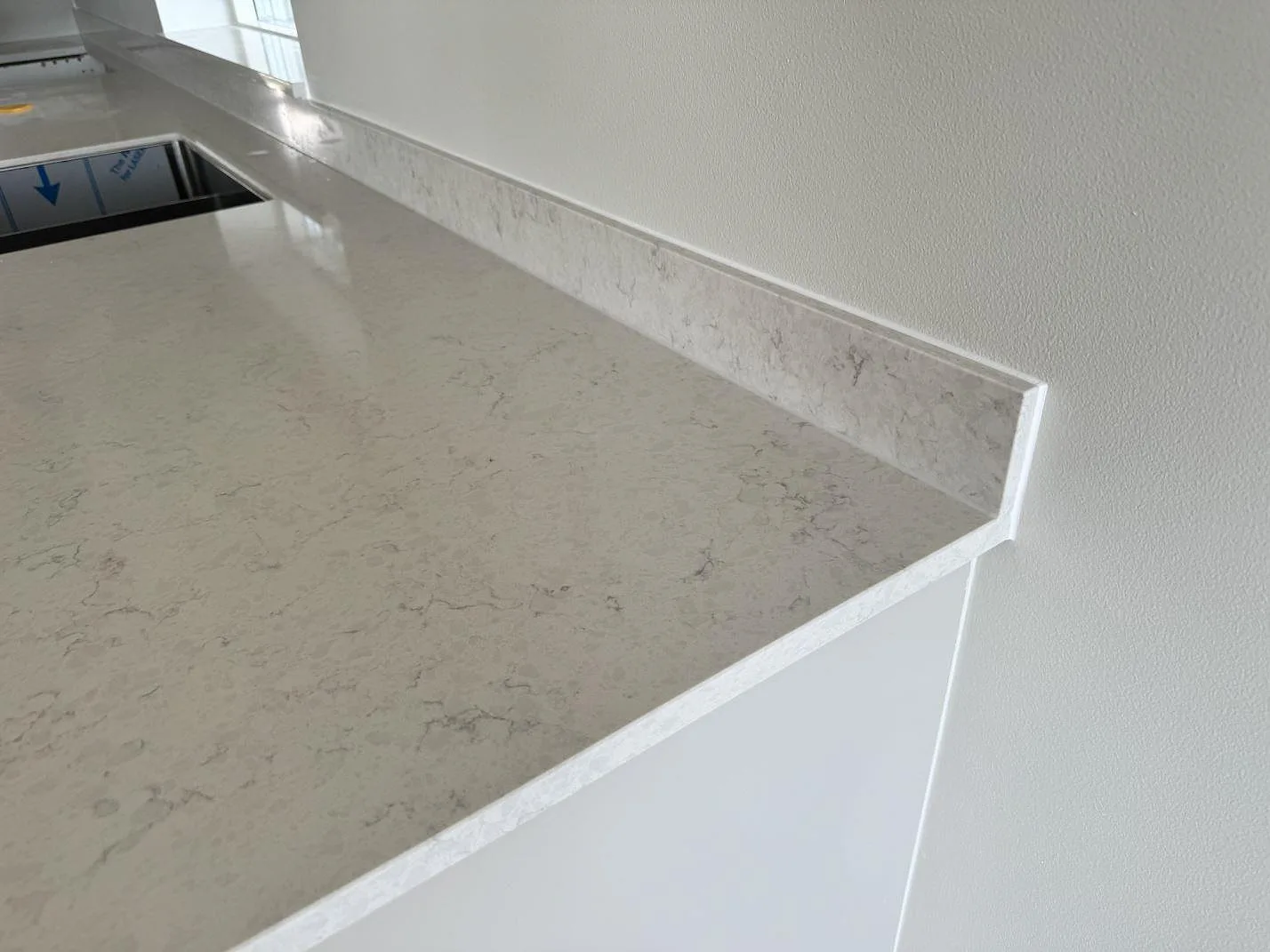 Detalj av polerad kompositbänkskiva i Silestone Snowy Ibiza med stänkkant och underlimmad diskho i Varberg.