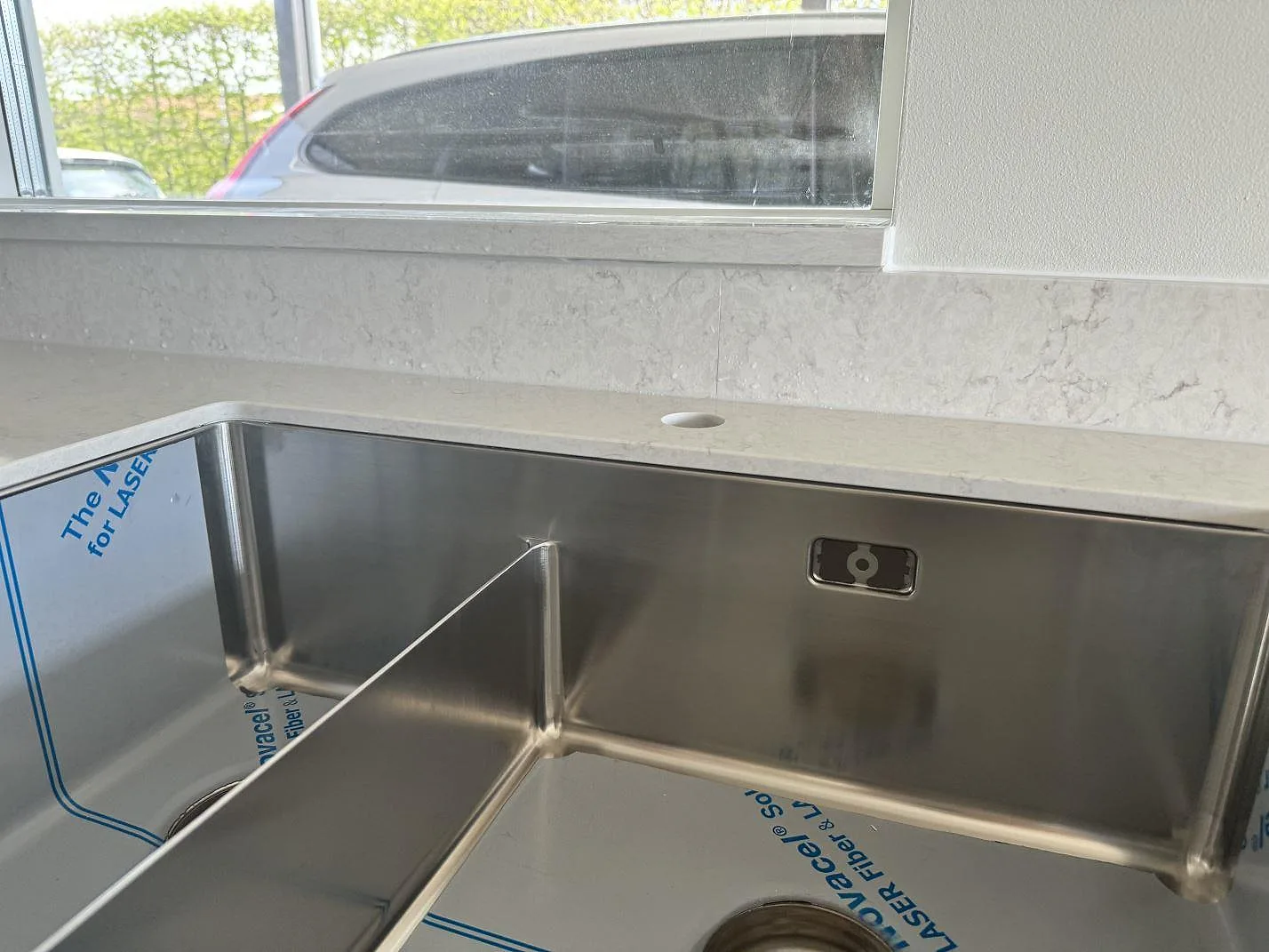 Närbild på underlimmad rostfri dubbelho, fönster och stänkskydd i polerad Silestone Snowy Ibiza i Varberg.