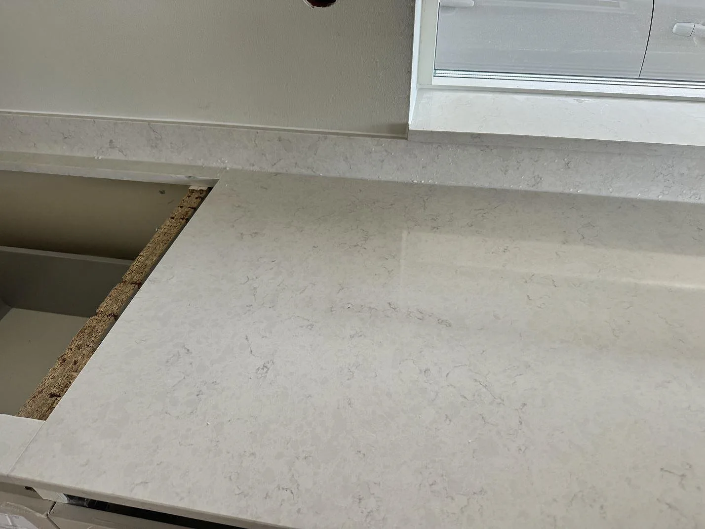 Polerad Silestone Snowy Ibiza runt öppning för häll vid fönster och uppvikt stänkkant i ett kök i Varberg.