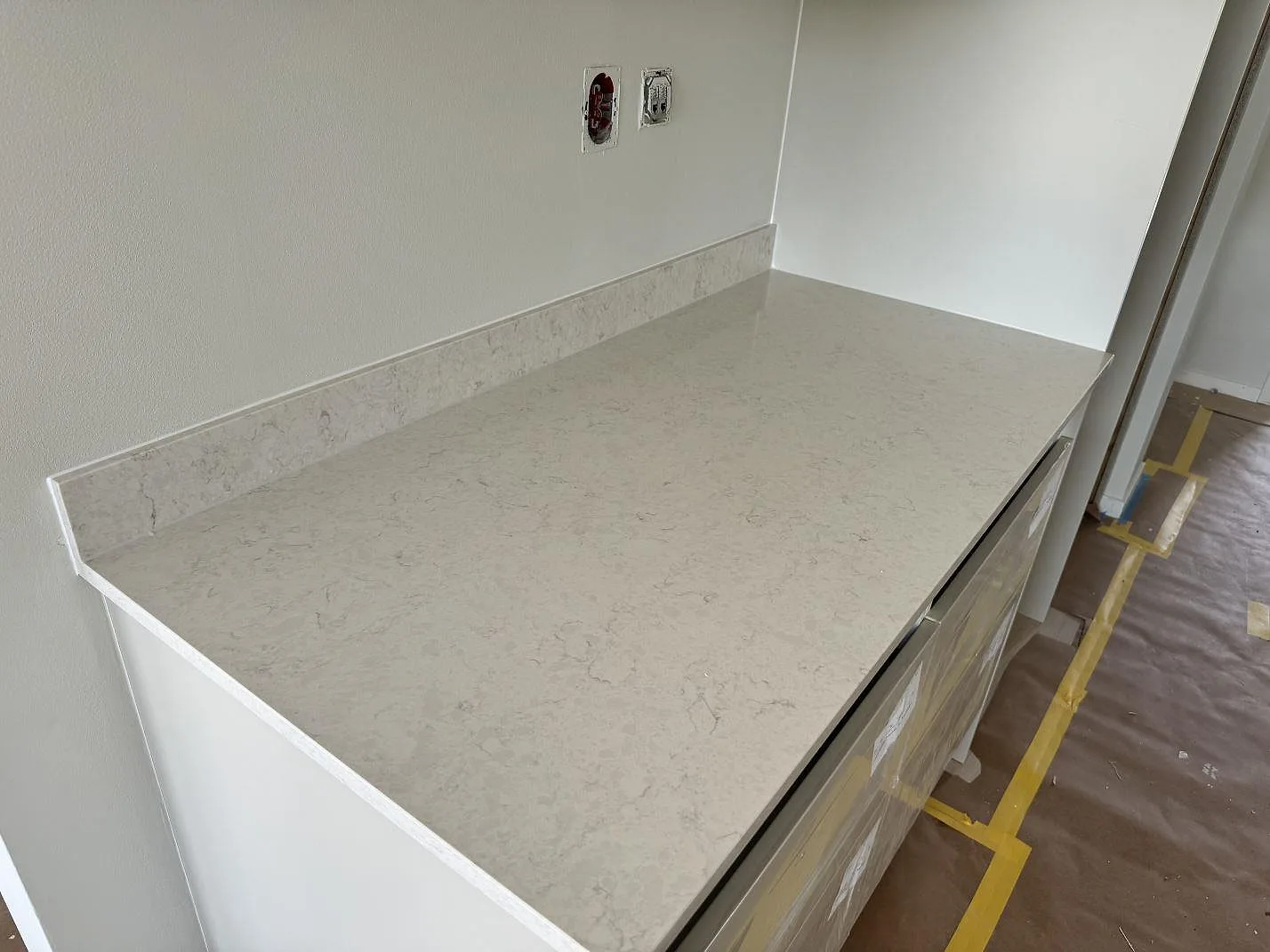 Polerad köksbänkskiva i Silestone Snowy Ibiza med ljus ådring och stänkkant på vita köksstommar i Varberg.