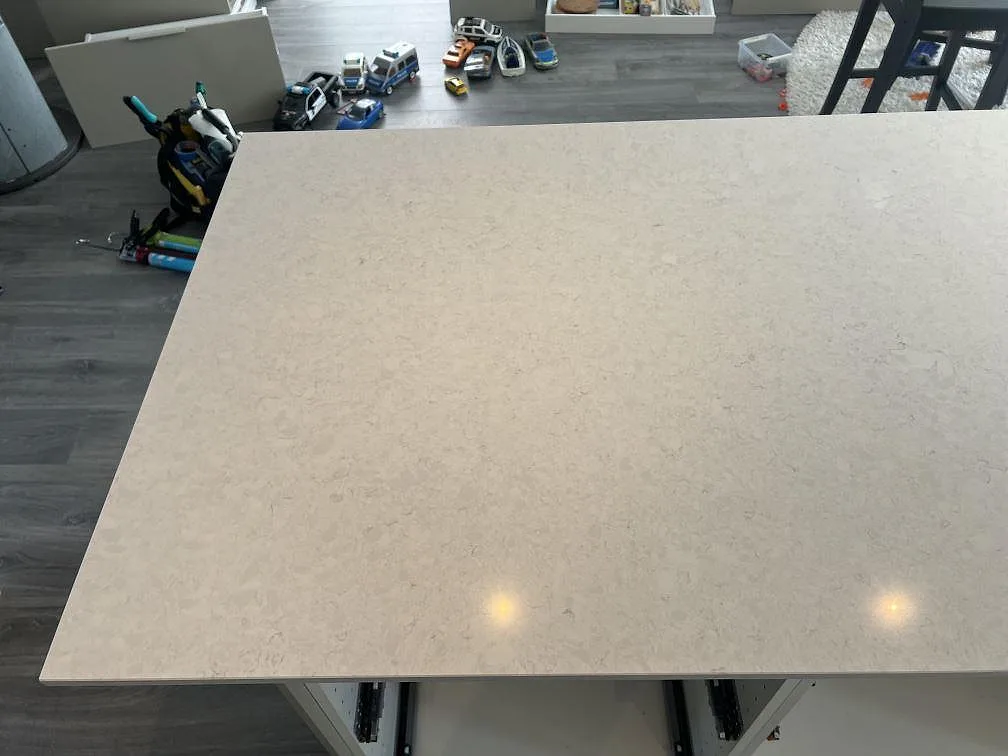 Köksö med polerad Silestone Snowy Ibiza kompositskiva, ljus ådring och öppna lådstommar under montering i Veberöd.