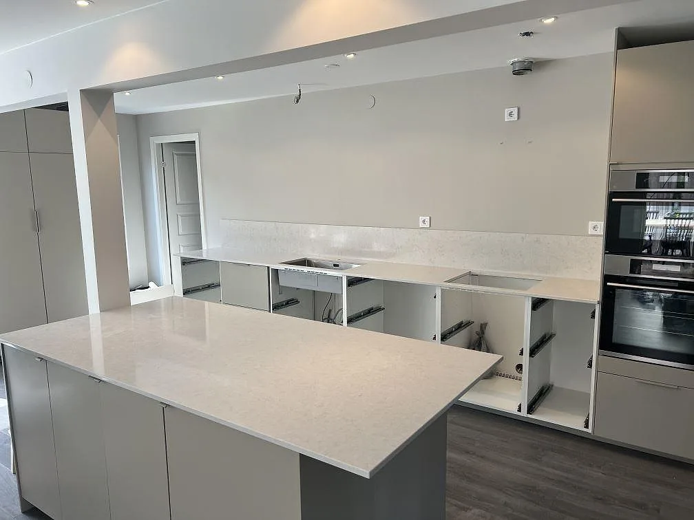 Köksbänkskiva i polerad Silestone Snowy Ibiza komposit med köksö, rak bänkrad och stänkskydd i ett kök i Veberöd.