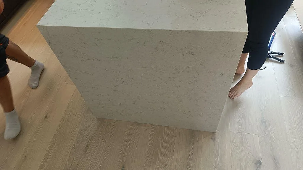 Köksö i polerad Silestone Snowy Ibiza med nedvikt sida mot trägolvet i ett kök under montering i Vellinge.