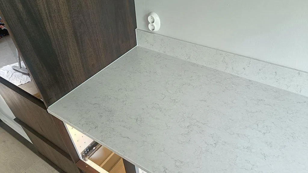 Köksbänkskiva i Silestone Snowy Ibiza med låg uppvikt stänkkant mot mörk träinredning i ett kök i Vellinge.
