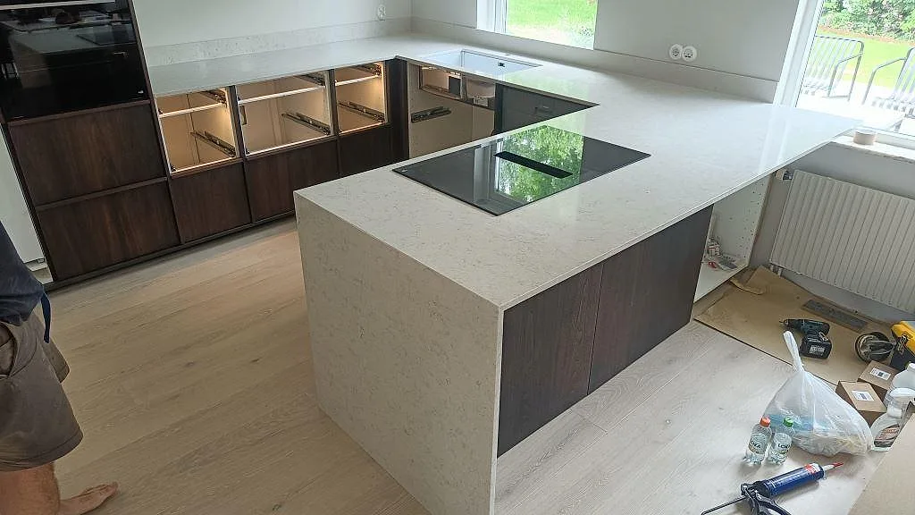 Köksbänkskiva i vit Silestone Snowy Ibiza, polerad, med köksö och infälld induktionshäll i ett U-format kök i Vellinge.