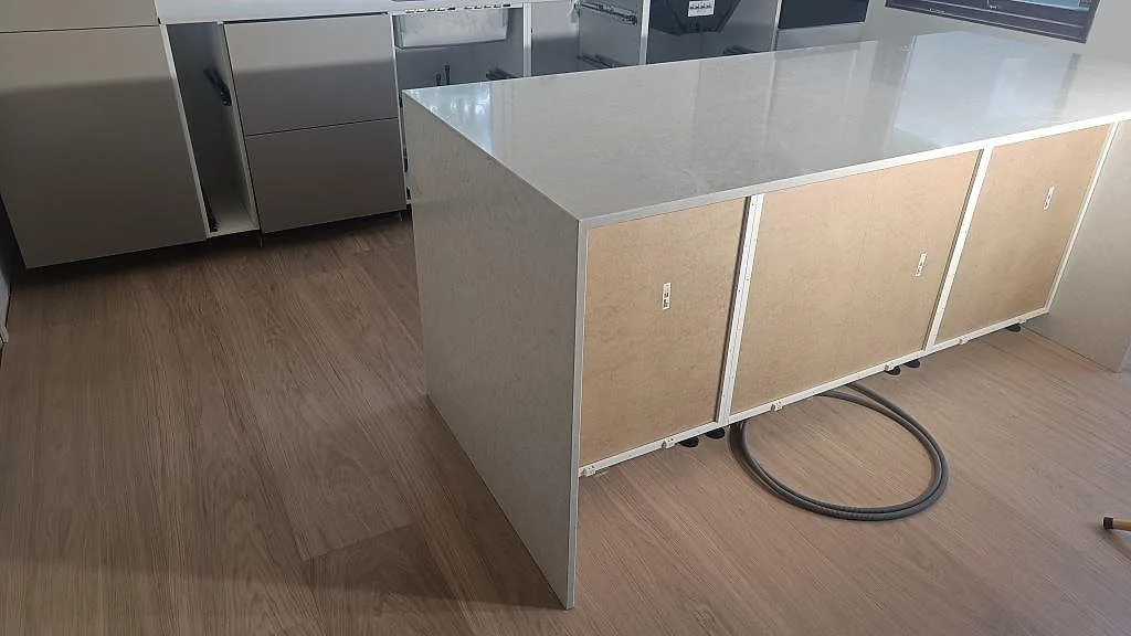 Köksö i polerad Silestone Snowy Ibiza med stenklädd gavel och blank ljus kvartskomposityta i ett kök under montering i Viken.