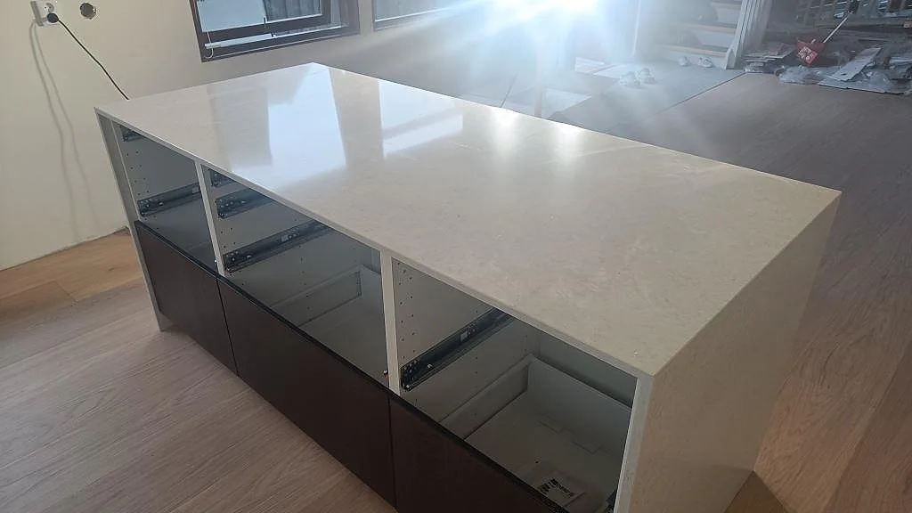 Polerad köksö i Silestone Snowy Ibiza med långa stenklädda sidor och öppna köksstommar under montering i Viken.