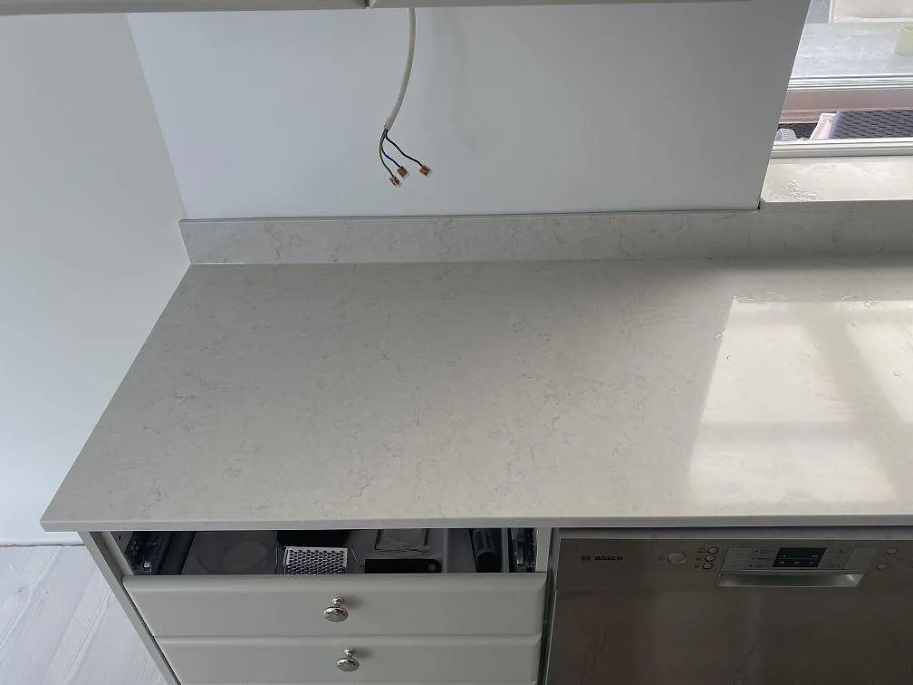 Rak bänkyta i polerad Silestone Snowy Ibiza med låg stänkkant, fönsterljus och diskmaskin under montering i Ystad.