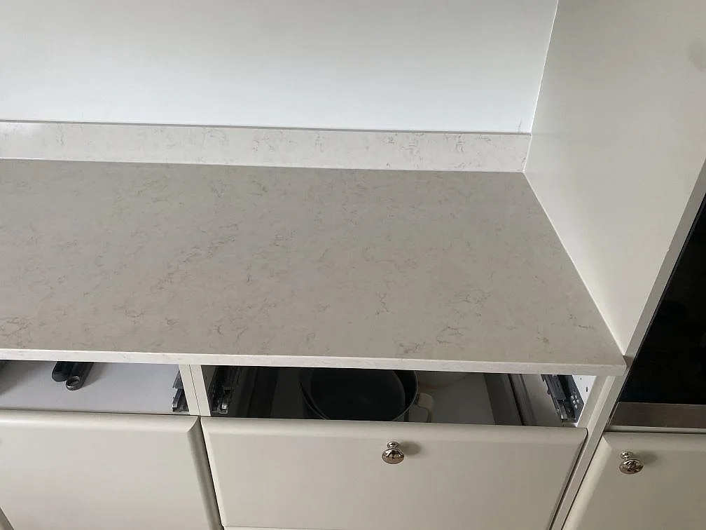 Hörndetalj av polerad Silestone Snowy Ibiza med ljus kompositådring, låg stänkkant och svart häll intill i Ystad.