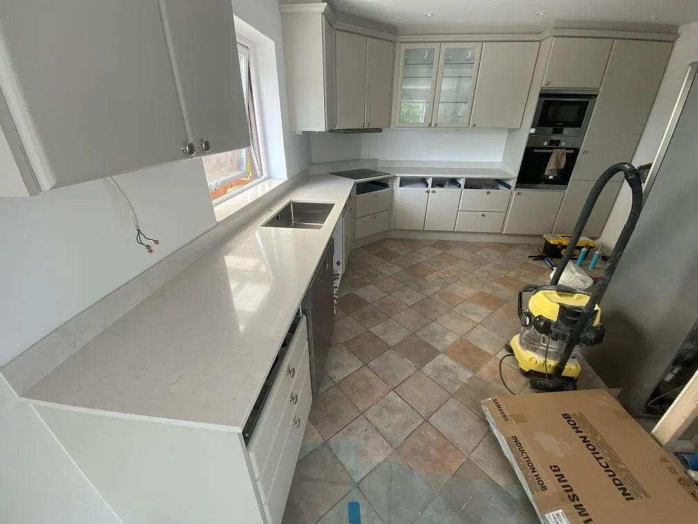 Polerad Silestone Snowy Ibiza som ljus köksbänk med låg stänkkant, rostfri diskho och öppna skåpstommar under montering i Ystad.