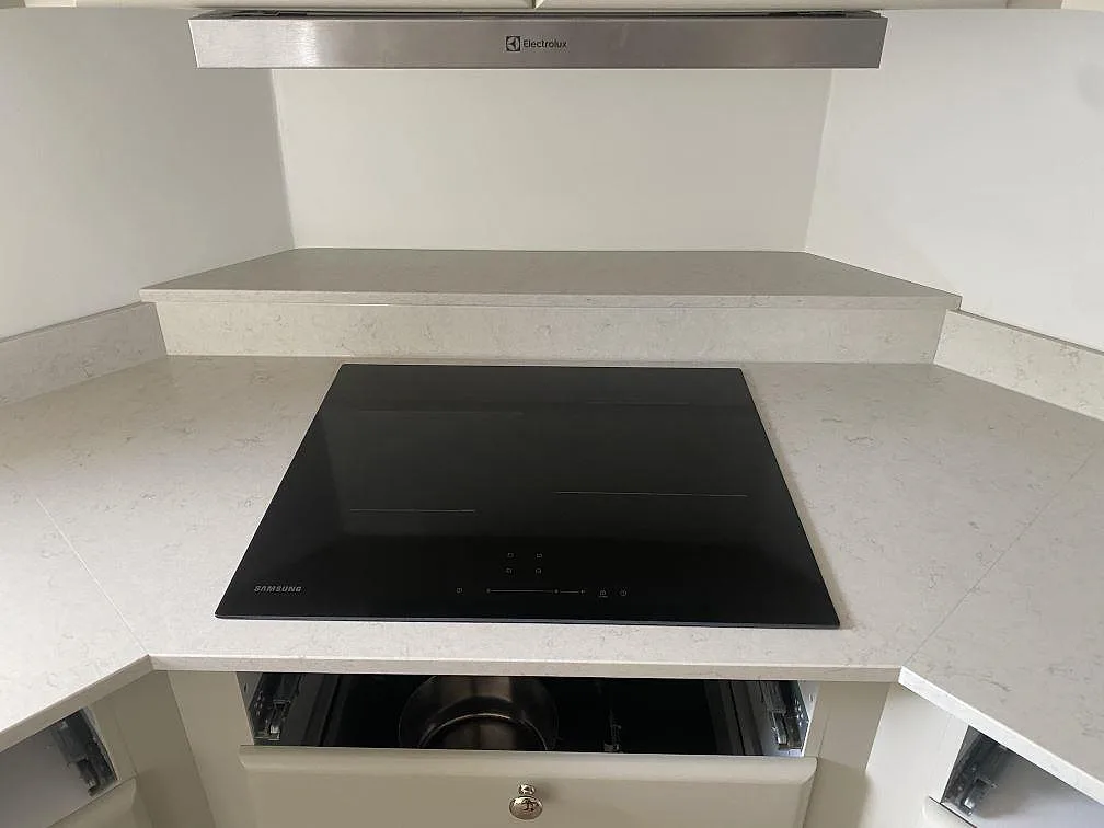 Svart induktionshäll i polerad Silestone Snowy Ibiza med uppvikt stänkkant och ljus ådring under fläkten i kök i Ystad.