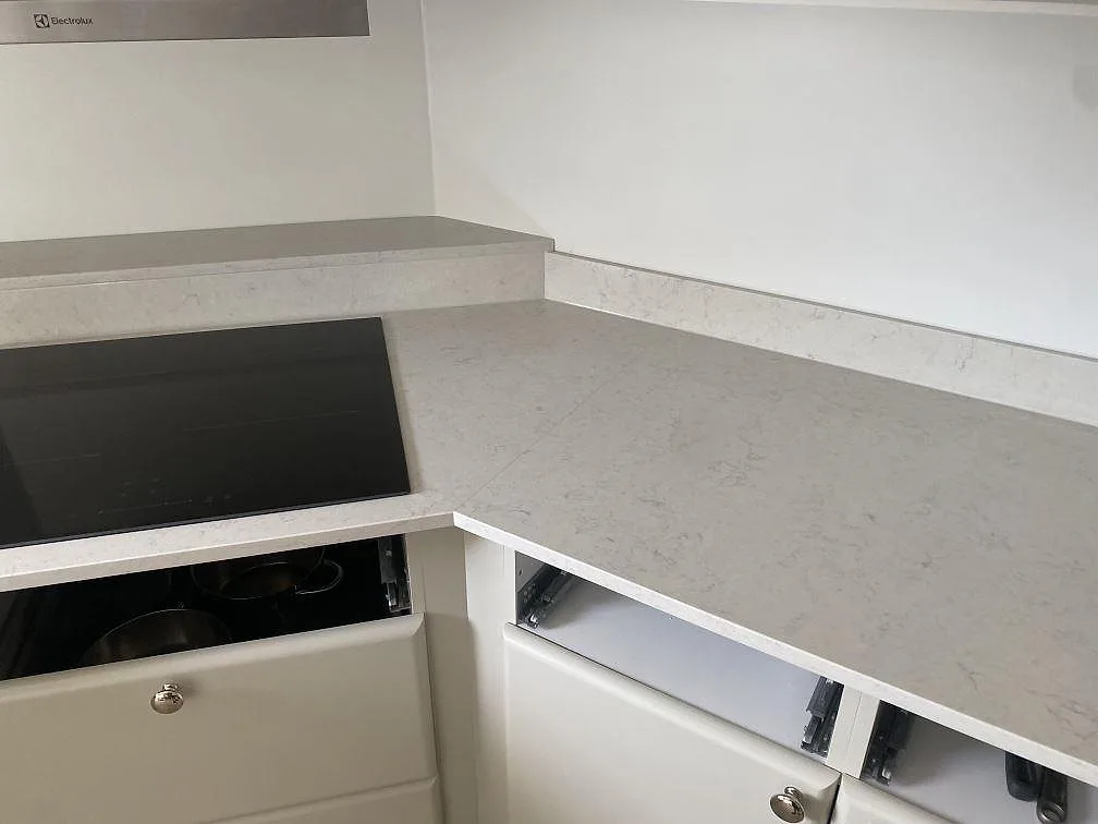 Närbild av hörnet på L-formad köksbänkskiva i polerad Silestone Snowy Ibiza med svart induktionshäll och låg stänkkant i Ystad.