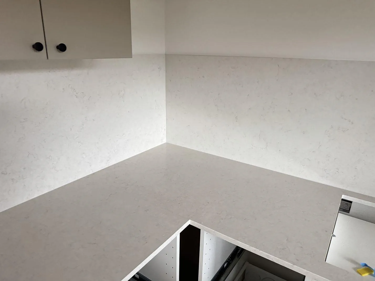 Hörnparti med polerad Silestone Snowy Ibiza som köksbänkskiva och stänkskydd, med öppen underskåpsstomme under montering i Ystad.