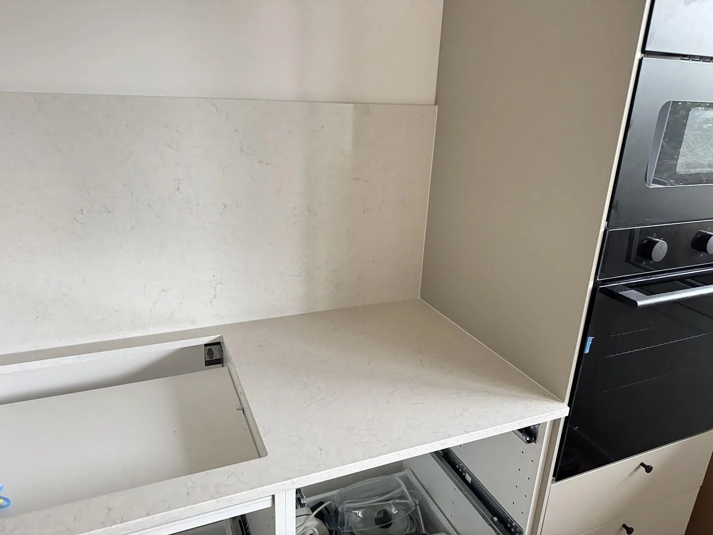 Ljus Silestone Snowy Ibiza-bänkskiva i komposit med rektangulärt hällurtag och inbyggnadsugn intill i ett kök under montering i Ystad.