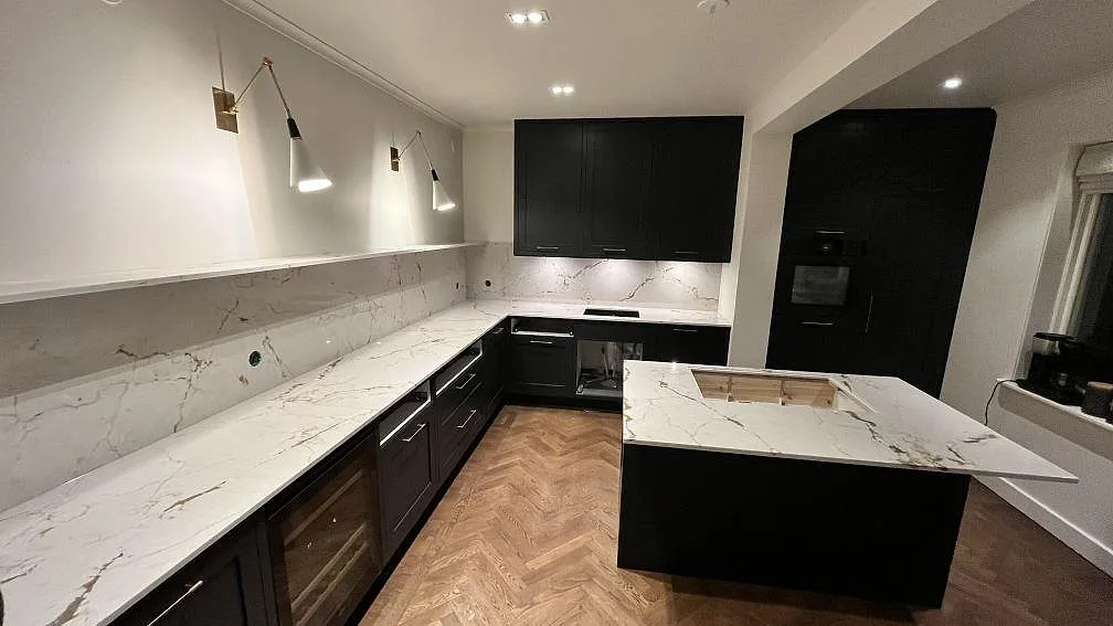 Polerad Silestone Versallies Ivory som köksbänkskiva med lång väggbänk, köksö och grå ådring i ett mörkt kök i Sigtuna.