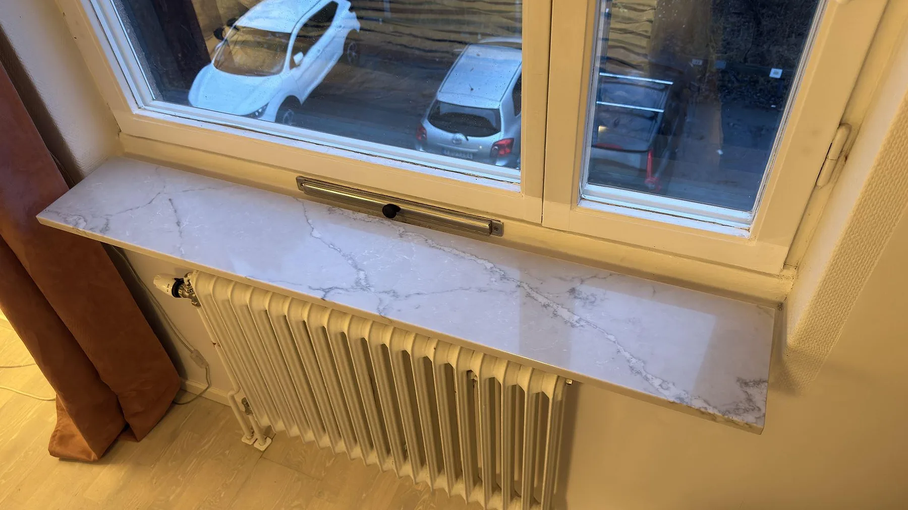 Polerad fönsterbänk i 20 mm Silestone Victorian silver med grå ådring över ett element i Bromma.
