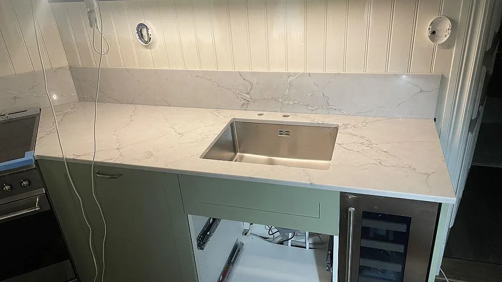 Polerad köksbänkskiva i Silestone Victorian silver med uppvikt stänkskydd och synlig diskhozon i ett kök under montering i Göteborg.