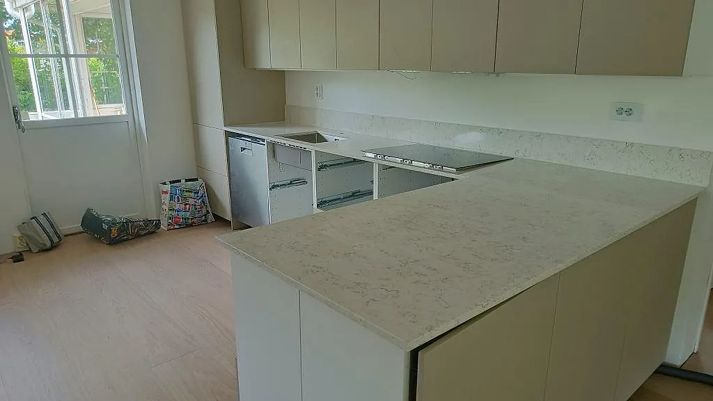 Köksbänkskiva i vit Silestone White Arabesque med mjuk grå ådring, polerad, vinklad bänk med uppvikt stänkkant, induktionshäll och diskhoplats i ett kök under montering i Göteborg.
