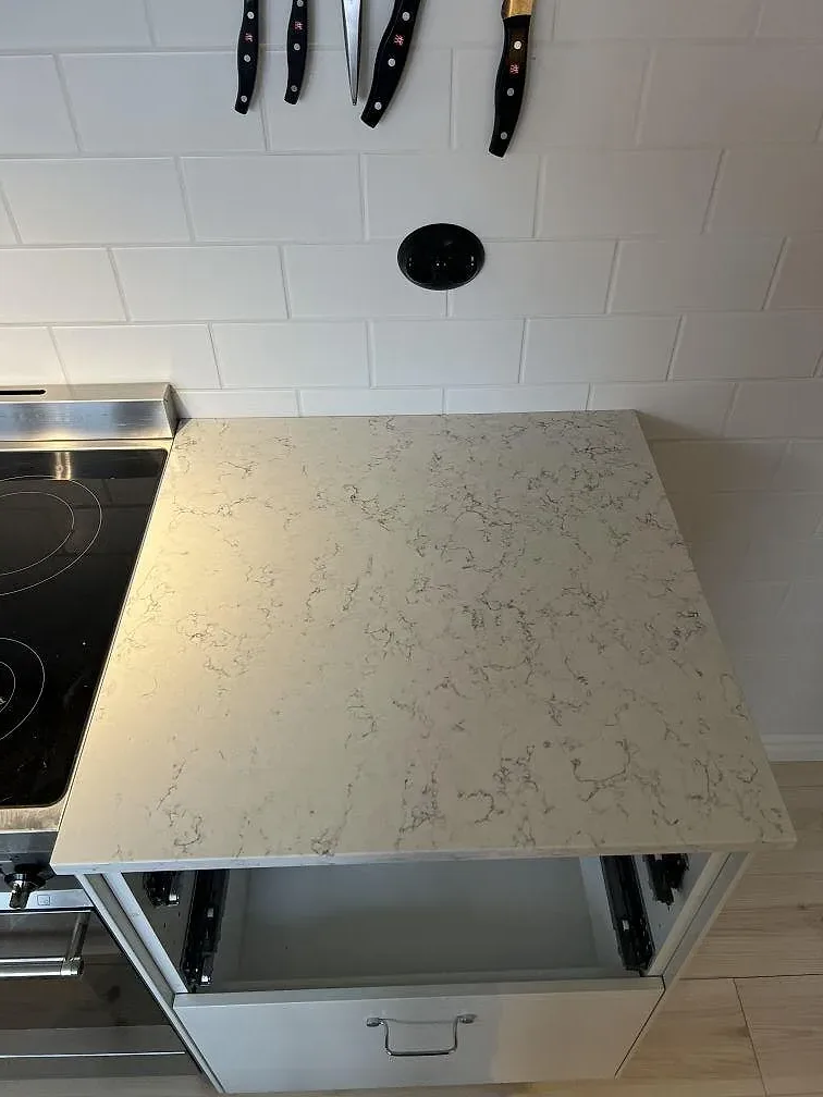 Sidovy av polerad Silestone White Arabesque vid fristående spis, vita väggplattor och köksinredning i Villands Vånga.