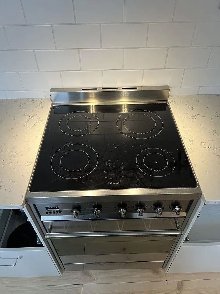 Polerad Silestone White Arabesque runt en fristående spis med rostfri front och vit kakelvägg i Villands Vånga.