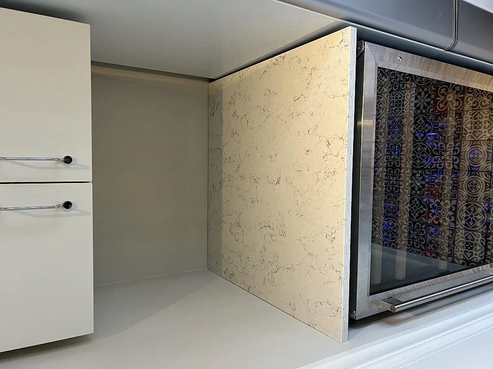 Kantsida och bänkskiva i polerad Silestone White Arabesque monterad intill fristående spis och vita lådor i Villands Vånga.
