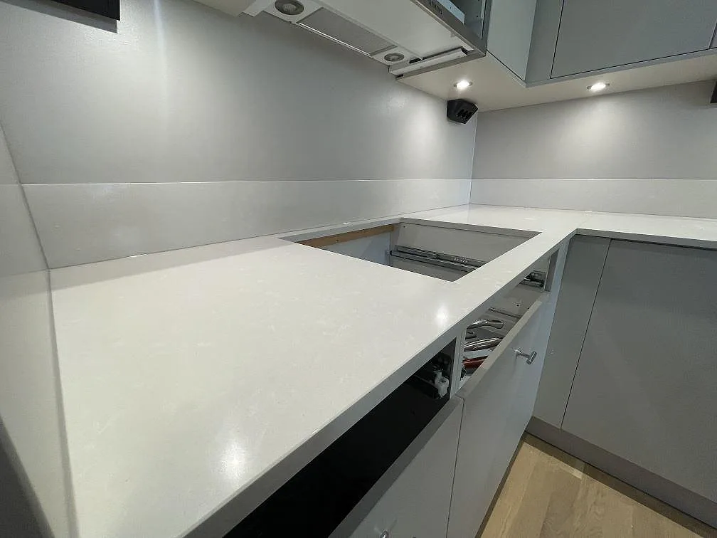 Närbild på polerad vit Silestone Yukon i kvartskomposit i ett kök i Örebro, med hällurtag, ljus kornighet och stänkskydd längs väggen.