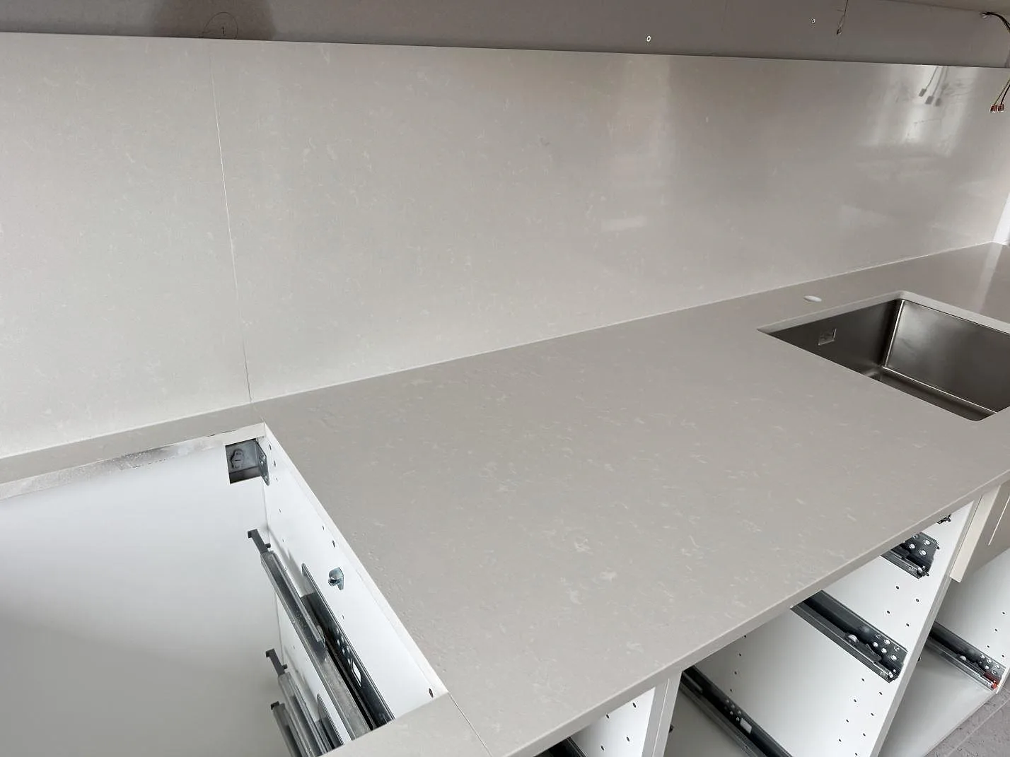 Ljus köksbänkskiva i Silestone Yukon, polerad komposit, med diskho och öppet skåp under montering i Råå.