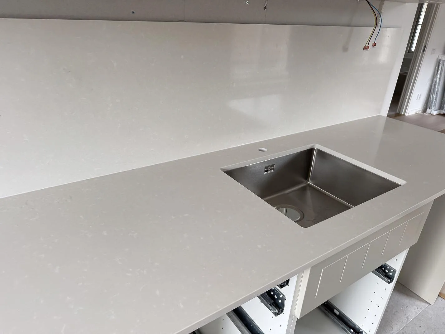 Polerad Silestone Yukon bänkskiva med rostfri diskho, kranhål och väggbeklädnad i ett kök i Råå.