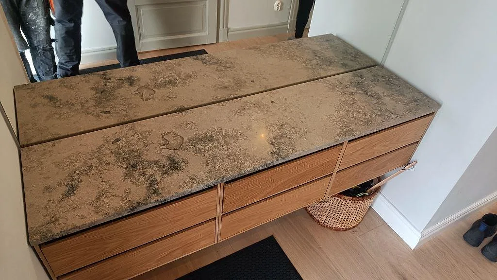 Bordsskiva i Jura Grey kalksten med matt yta och fossilådring, monterad på ett ekskåp i en hall i Sjömarken.